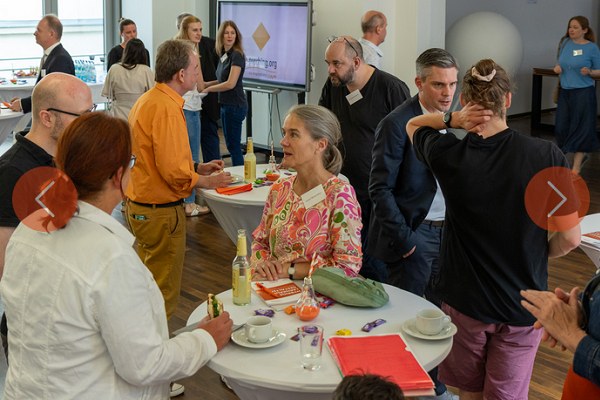 Bildergalerie zur Jubiläumstagung Menschen in festlicher Kleidung stehen um Stehtische herum und unterhalten sich.