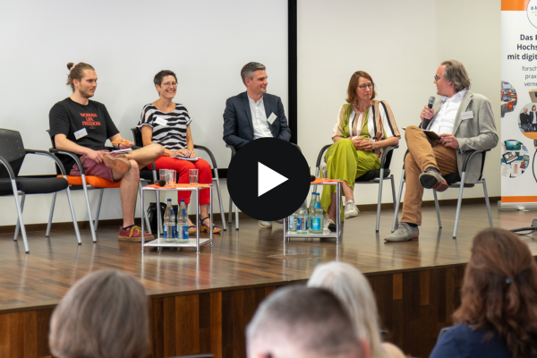 Jubiläumstagung - Fishbowl Auf dem Podium sitzen fünf Personen auf Stühlen. Ganz rechts sitzt der Moderator Johannes Moskaliuk mit einem Mikrofon in der Hand und wendet sich seinen vier Podiumsgästen zu.